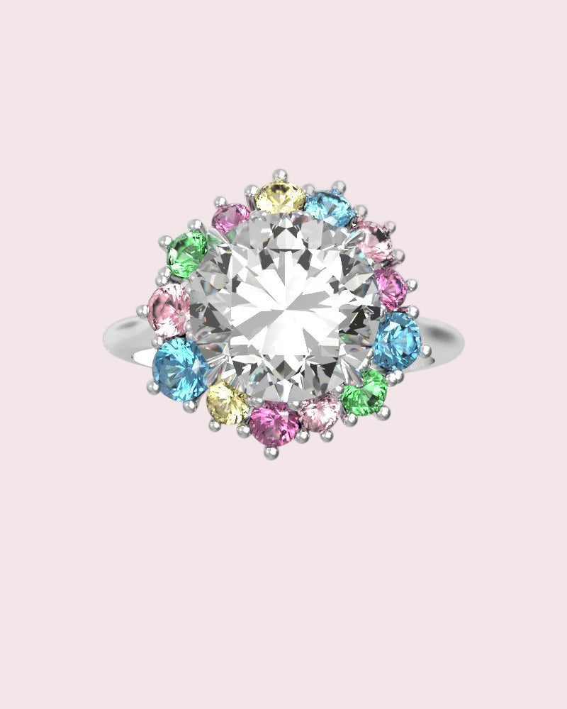 White gold ring featuring a large clear round center stone surrounded by a halo of small multicolored gemstones in pink, blue, green, and yellow, set against a clean white background.